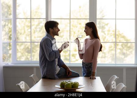 Felice cute millennial maschio e femmina caucasico con bicchieri bere vino in data a casa in cucina Foto Stock