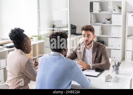 Giovane coppia afroamericana che ascolta il consulente finanziario barbato alla consultazione in carica Foto Stock