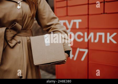 La donna raccoglie la posta dalla macchina automatica self-service del terminale postale sulla strada. Servizio di spedizione pacchi o concetto di imballaggio per la consegna Foto Stock