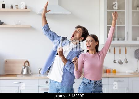 Felice emotivo divertente millenario europeo signora e ragazzo hanno divertimento insieme, cantando canzone al microfono immaginario Foto Stock