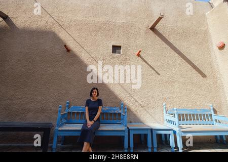 Donna felice seduta su panchina in strada della città vecchia di Bur Dubai vicino Creek distretto. Idee di viaggio Foto Stock