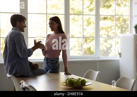 Sorridente uomo e donna millennial europeo clink occhiali in data sensazione felice insieme in cucina interni Foto Stock