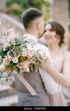 Sposa con un bouquet abbracci sposare sui gradini di pietra. Verticale Foto Stock