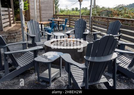 Vista ravvicinata delle sedie adirondack che circondano una fossa di fuoco piena di pietre all'interno di un patio all'aperto in un ristorante Foto Stock