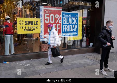 Uno shopper passa accanto al negozio Urban Outfitters di Oxford Street, dove i poster pubblicizzano il Black Friday, il 29 novembre 2021, a Londra, in Inghilterra. Foto Stock