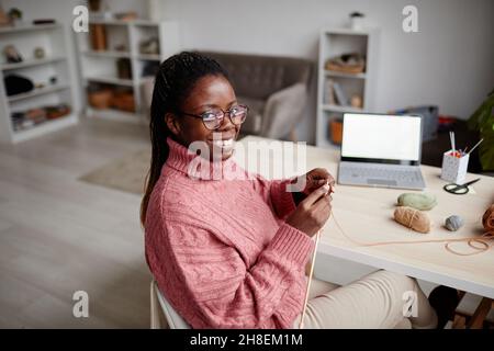 Ritratto della giovane donna afroamericana che si inginocchiava a casa e sorride alla macchina fotografica, spazio copia Foto Stock