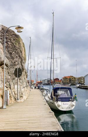 Smögen, Svezia - 9 giugno 2021: Ponte in legno lungo l'acqua chanel sull'isola con barche a vela e case sul lato opposto Foto Stock