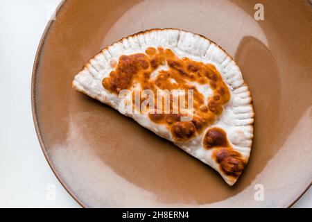 Il cheburek fritto giace su un piatto marrone su sfondo bianco. Foto Stock