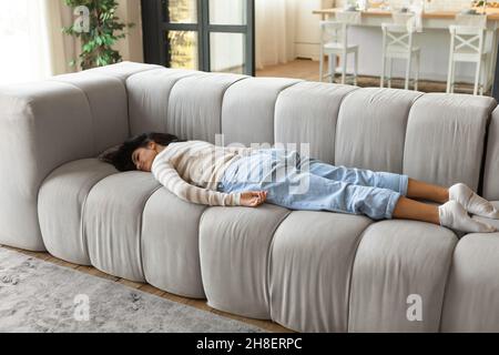 Giovane donna bruna stanca che dorme sul divano durante il giorno, si sente esausta, prendendo il pisolino a casa, spazio copia Foto Stock