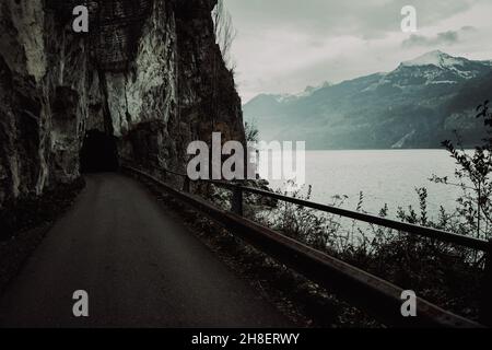 Scenario inquietante di una strada che conduce in un tunnel in una scogliera presso il lago di Walenstadt in Svizzera Foto Stock