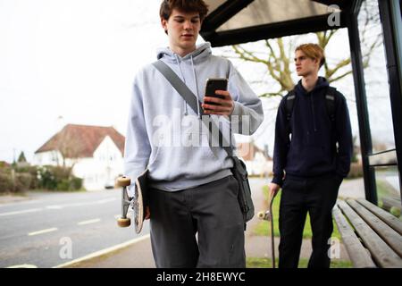 Ragazzi adolescenti con skateboard e smartphone alla fermata dell'autobus Foto Stock