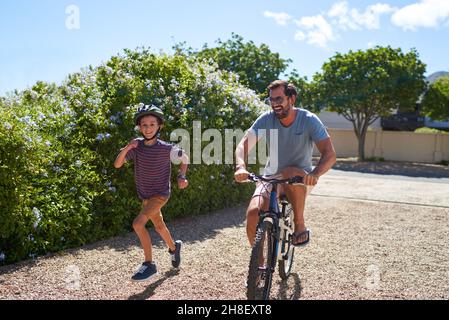 Felice padre e figlio correre e andare in bicicletta in un vialetto soleggiato Foto Stock