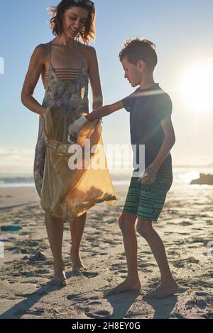 Madre e figlio che si dedicano al volontariato raccogliendo rifiuti sulla spiaggia soleggiata Foto Stock