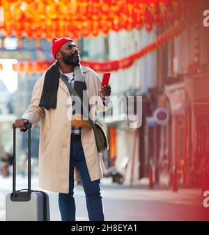 Turista maschile con smartphone e valigia sul marciapiede della città Foto Stock