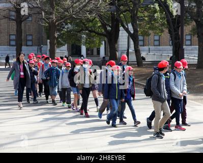 Un gruppo di bambini con insegnante in partenza dal Museo Nazionale di Tokyo in Ueno Park, Tokyo indossando abiti casual e berretti rossi. Foto Stock