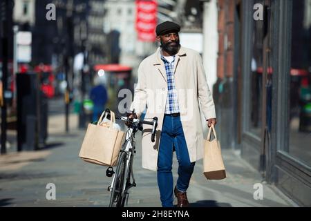 Uomo con biciclette e borse di alimentari a piedi nella città soleggiata Foto Stock