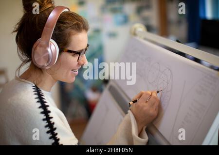Architetto femminile con cuffie che disegna progetti Foto Stock