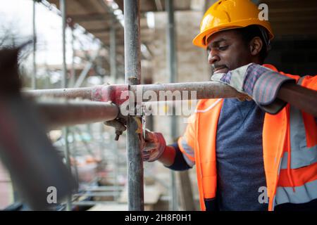 Lavoratore di costruzione maschile che monta impalcature in cantiere Foto Stock
