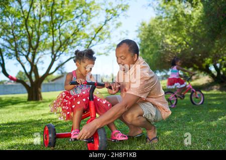 Nonno che aiuta la nonna a fare un giro in triciclo nel parco estivo Foto Stock