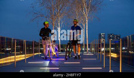 Uomini con biciclette su percorso illuminato in città di notte, Londra, Regno Unito Foto Stock