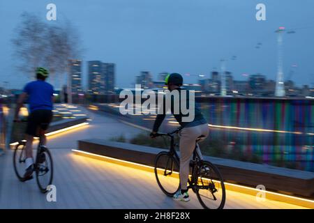 Uomini in bicicletta sulla passerella illuminata in città di notte, Londra Foto Stock