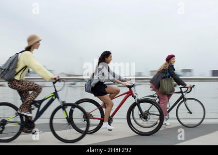 Giovani donne amici che cavalcano biciclette lungo il lungomare Foto Stock