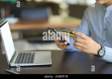 Immagine ritagliata di un uomo d'affari o di un uomo d'affari che detiene carta di credito e smartphone alla sua scrivania. internet online banking concetto. Foto Stock
