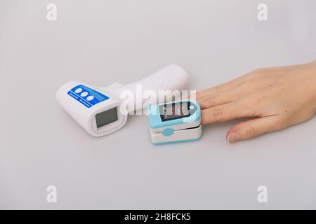 Pulsossimetro e termometro a pistola su sfondo bianco. Misurazione della saturazione dell'ossigeno, della frequenza del polso e dei livelli di ossigeno. Termometro a pistola isometrica a infrarossi Foto Stock