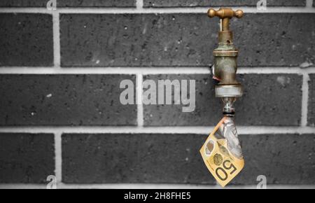 Un rubinetto esterno di ottone o rubinetto con una nota di 50 dollari che esce da esso come acqua. Sfondo in mattoni bianchi e neri. Foto Stock