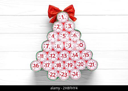 Calendario dell'avvento in forma di albero di Natale con numeri e nastro invece di stella su tavola bianca di legno Calendario dell'avvento Natale concetto Vista dall'alto piatto Foto Stock