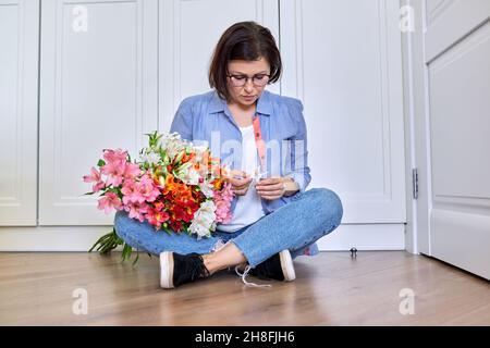 Triste turbata donna di mezza età con un bouquet di fiori Foto Stock