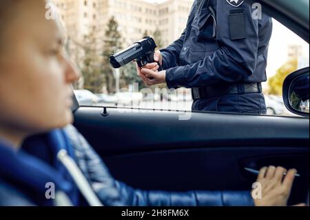 Ufficiale di polizia maschile con pistola arresta autista femminile Foto Stock