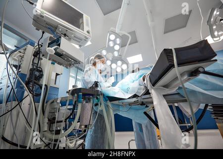 chirurgo che tiene traccia delle funzioni vitali del corpo durante la chirurgia cardiaca. Chirurgo che guarda il monitor medico durante l'intervento chirurgico. Medico controllo monito Foto Stock