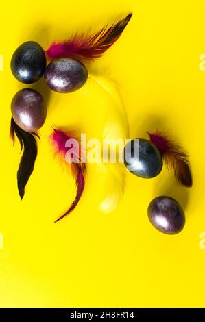 Composizione pasquale creativa. Uova viola e piume su sfondo giallo. Vista dall'alto. Disposizione piatta Foto Stock