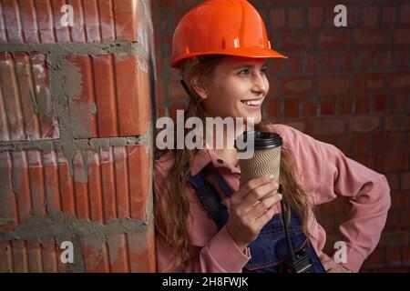 Donna di buona qualità in uniforme da costruzione in posa con tazza di caffè Foto Stock