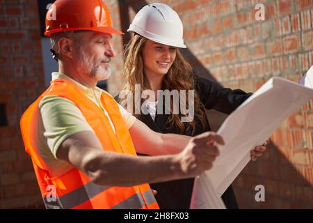 Costruttori entusiasti che guardano alle stampe bianche e sorridenti delle costruzioni Foto Stock