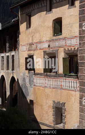 Tipica casa familiare a tre piani nel villaggio della bassa Valle Engadina di Ardez, Graubünden o Grigioni cantone, Svizzera orientale. Il fronte color albicocca ha decorazioni dipinte su due livelli che simulano balconi e un'iscrizione da parte di una finestra superiore in Rhaeto-Romance o Romansh, la lingua ancora parlata da molti abitanti locali. Foto Stock