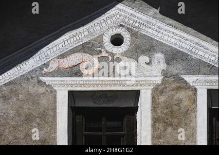 Una sirena di buxom si distende sopra una finestra accanto a un mostro di mare scottante con una coda a forcella e una lingua a freccia in accattivante arte sgraffito rustico su una casa di famiglia tradizionale restaurata in Ardez, Graubünden o Grigioni cantone, Svizzera orientale. Draghi, sirene e creature marine si trovano in molte abitazioni della zona restaurate da artisti locali sgraffiti all'inizio del 1900. Foto Stock