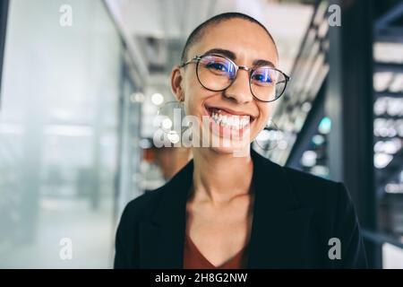 donna d'affari che sorride allegramente alla telecamera. Giovane donna d'affari felice in piedi da sola in un posto di lavoro moderno. Giovane donna d'affari di successo che lavora Foto Stock