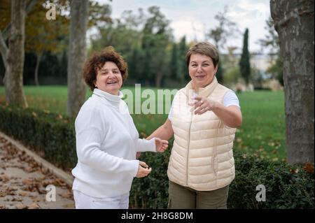 Due donne anziane all'aperto. Due donne anziana che parlano. Due vecchi amici che chiacchierano nel parco. Sorridenti donne di mezza età che parlano all'aperto. Guardando il camer Foto Stock