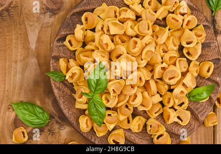 Tortellini su tavola di legno con basilico e parmigiano. Specialità della cucina bolognese ed emiliana: Cappelletti, pasta fresca all'uovo con ripieno di carne e verdure. Sopra . Posiziona per testo Foto Stock