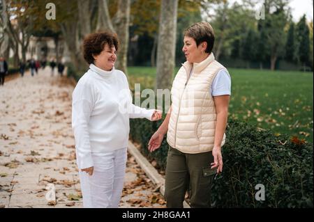 Due donne anziane all'aperto. Due donne anziana che parlano. Due vecchi amici che chiacchierano nel parco. Sorridenti donne di mezza età che parlano all'aperto Foto Stock