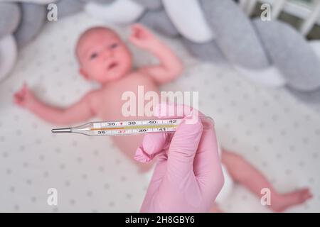 Il bambino nel presepe misura la temperatura corporea. La mamma misura la  temperatura corporea del bambino con un termometro Foto stock - Alamy