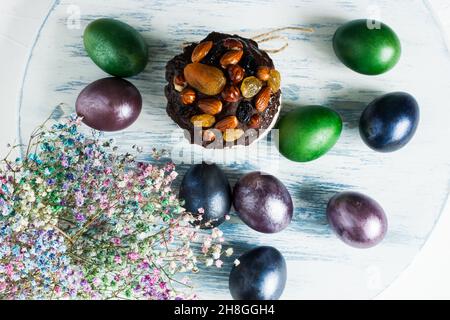 Vista dall'alto dello sfondo di legno blu con torta di Pasqua, uova colorate e fiori di primavera Foto Stock