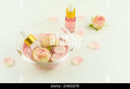 olio cosmetico di rose in bottiglie con pipetta in recipiente di vetro su un tavolo di legno bianco. il concetto di auto-cura naturale Foto Stock