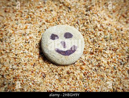 Le facce dipinte di Smiley sui ciottoli alla spiaggia estiva Foto Stock