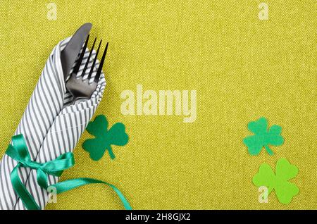 Set di posure piatte per la giornata di San Patrizio con forchetta argenteria, cucchiaio e tovagliolo su un placemat verde, con spamogli fatti a mano in feltro. Spazio di copia Foto Stock