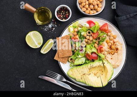 Insalata sana vegana bilanciata con hummus di ceci, avocado, pomodori e foglia verde insalata. Vista dall'alto spazio di copia su sfondo nero Foto Stock