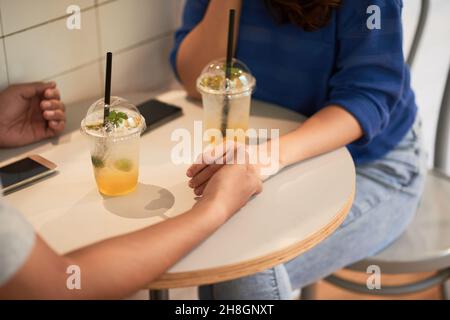 Primo piano di una coppia irriconoscibile che tiene le mani sul tavolo con limonata e smartphone in caffetteria Foto Stock