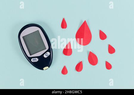 Dispositivo misuratore di zucchero nel sangue per la malattia del diabete accanto a gocce di sangue di carta Foto Stock